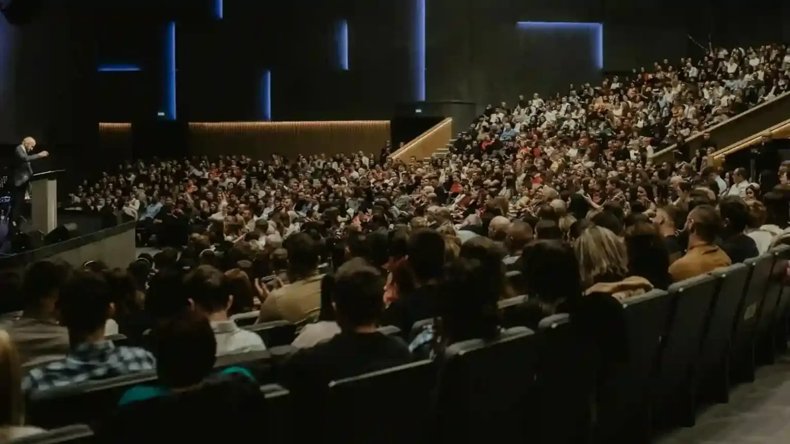 Conférences avec Un grand nombre de personne est rassemblé dans un hémicycle aux couleurs marrons et écoute un speaker sur scène
